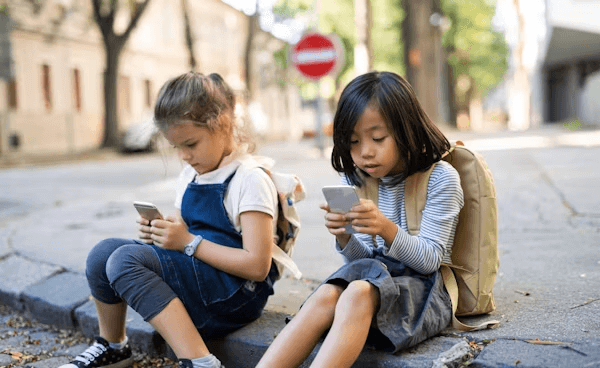 kids sitting on the street playing with phones